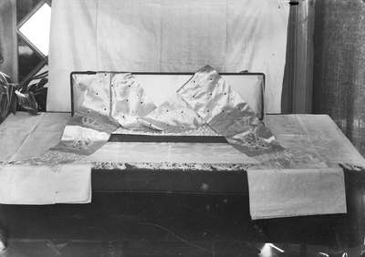 853683 Afbeelding van een zijden sjerp (?) met de letters NV VM (?) in een koffer met een label van de firma C.J. ...